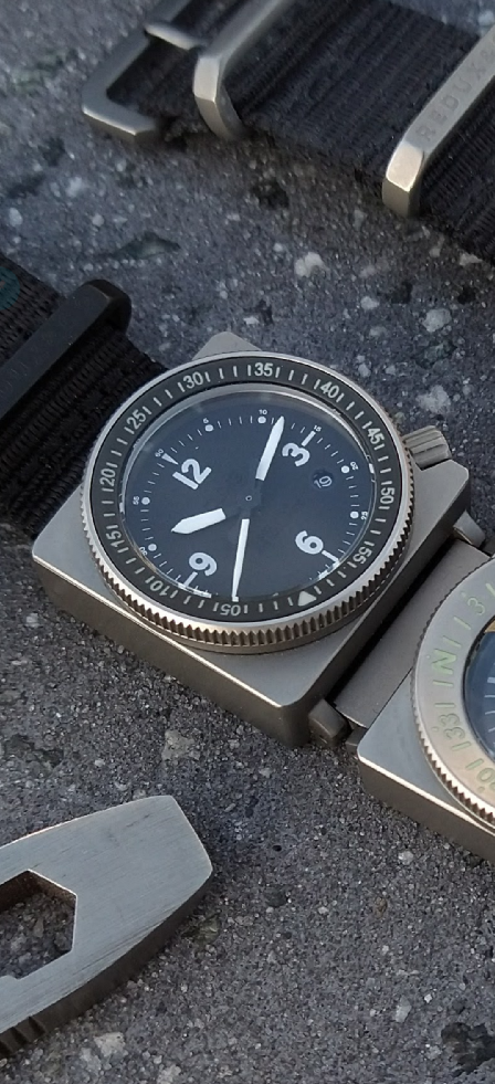 SCOUT A-9 Automatic with compass module and titanium hardware on textured ground.