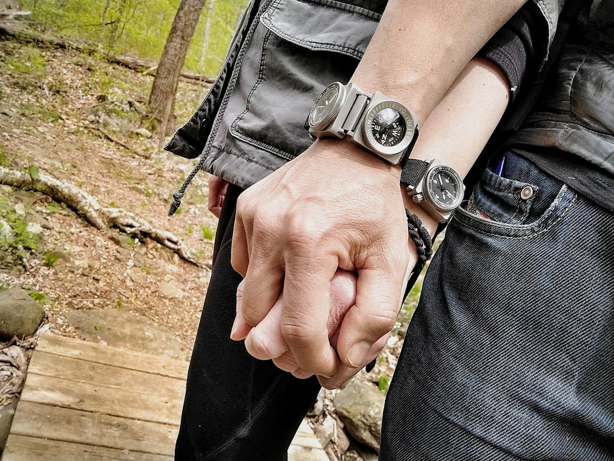 Two SCOUT wearers holding hands outdoors, showing the compact system across different wrists.